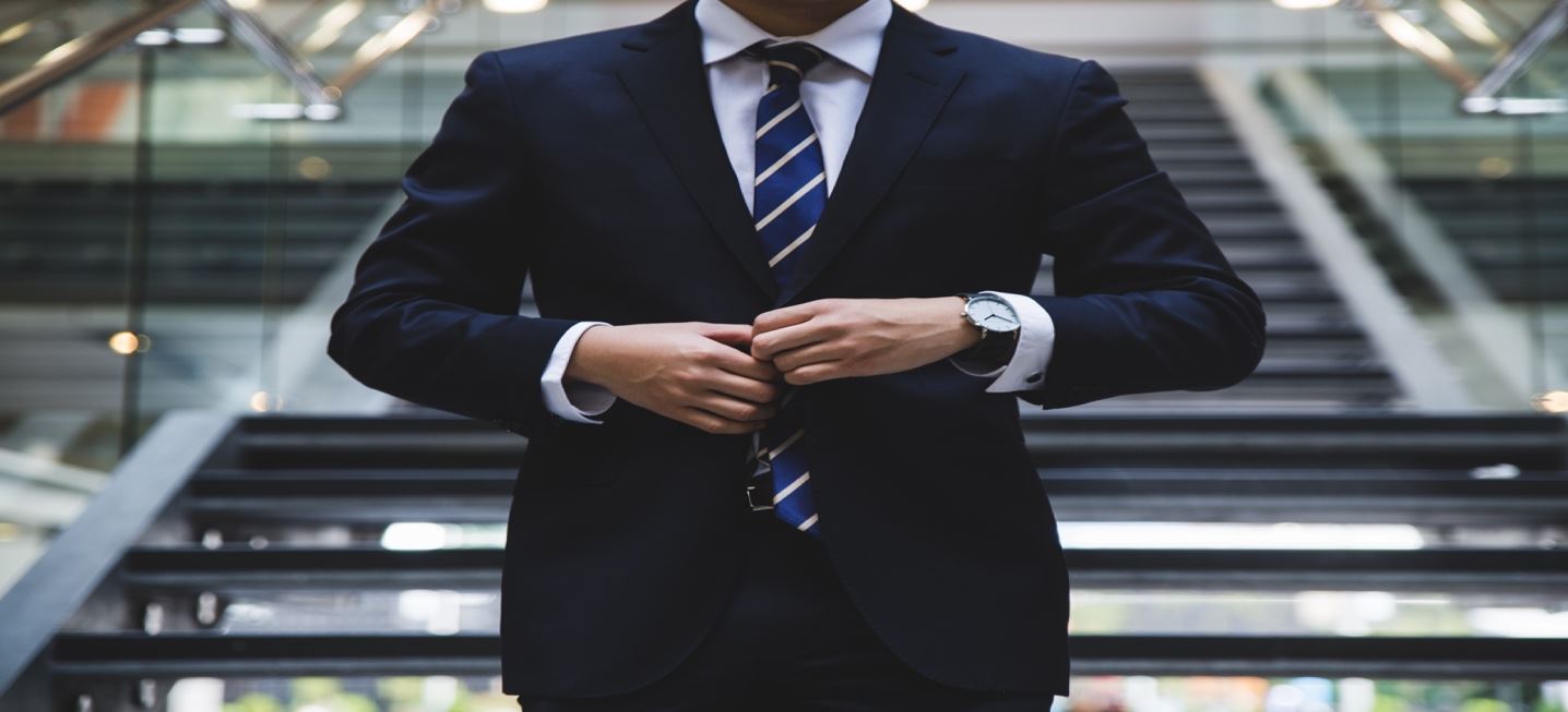 A person in a suit buttoning his jacket

Description automatically generated